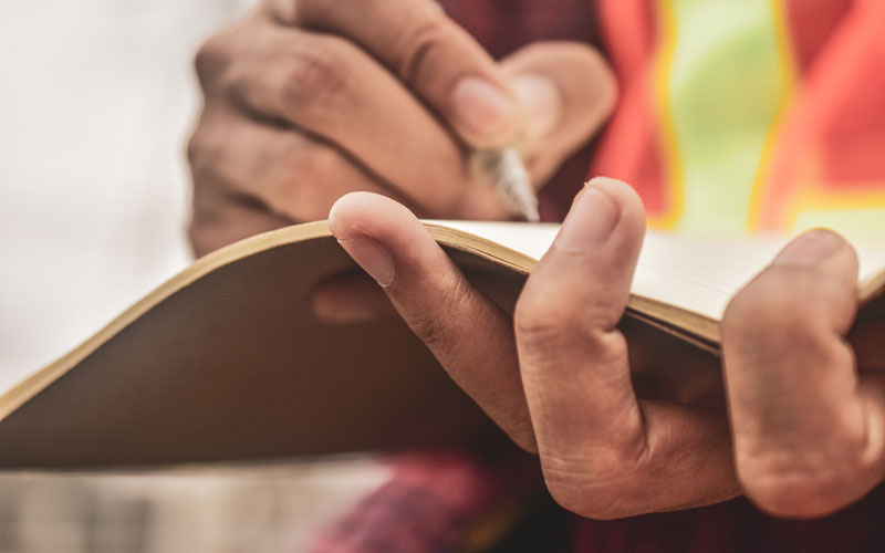 A persons hands on a notebook conducting a survet and recording notes